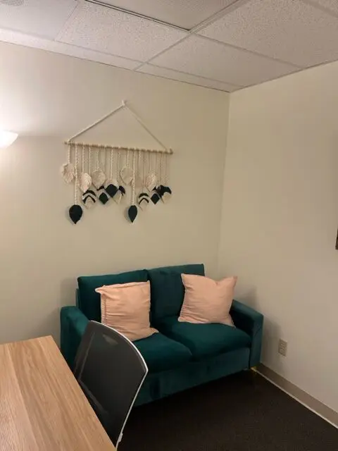 Office with comfortable seating and a knitted hanging art piece on the wall.